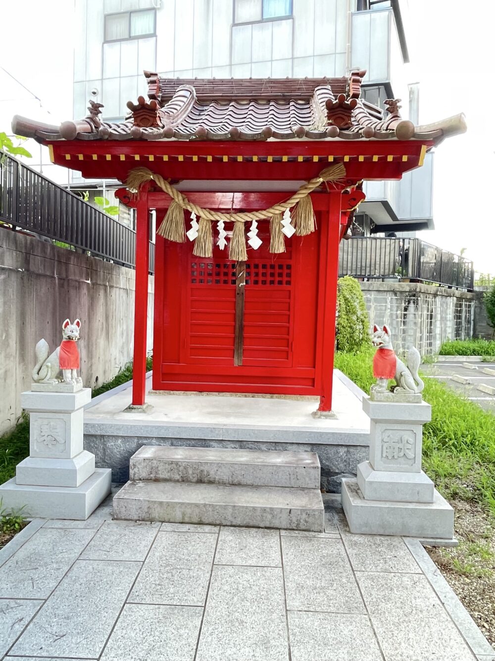 朱塗りの社と、左右に配された赤い前掛けをつけた狐像（伊賀八幡宮境内の稲荷社）