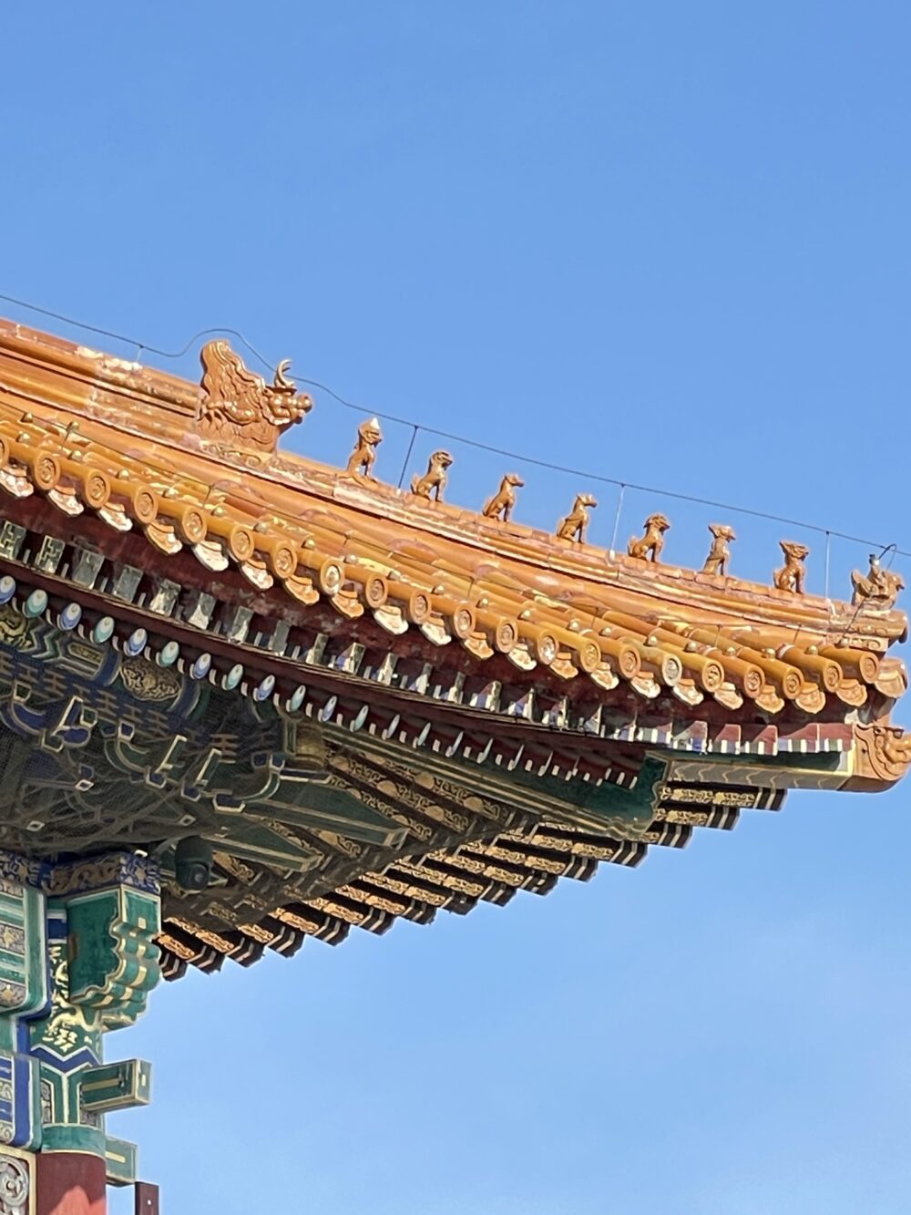 紫禁城の屋根の端に並ぶ屋脊走獣。先頭に仙人騎鳳が立ち、龍・鳳・獅子・天馬・海馬・狻猊・押魚などの神獣が続く伝統配置。金色の瓦が青空に映える。