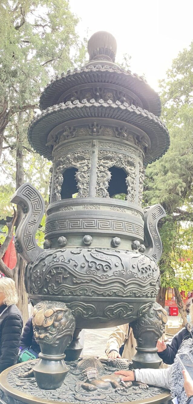 御花園に置かれた大型の銅製香炉の全景。精巧な龍や雲文の装飾が施され、獅子の脚部分に多くの観光客が手を触れている様子。