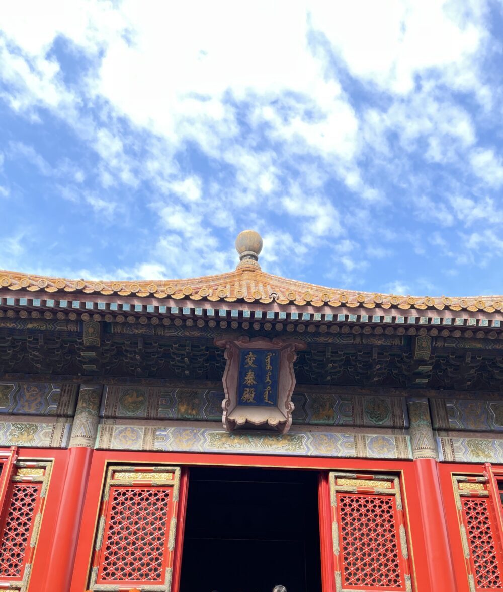 交泰殿の正面外観。金瓦の屋根と華やかな彩色が施された梁、赤い格子扉が青空に映え、入口には多くの観光客が集まっている。