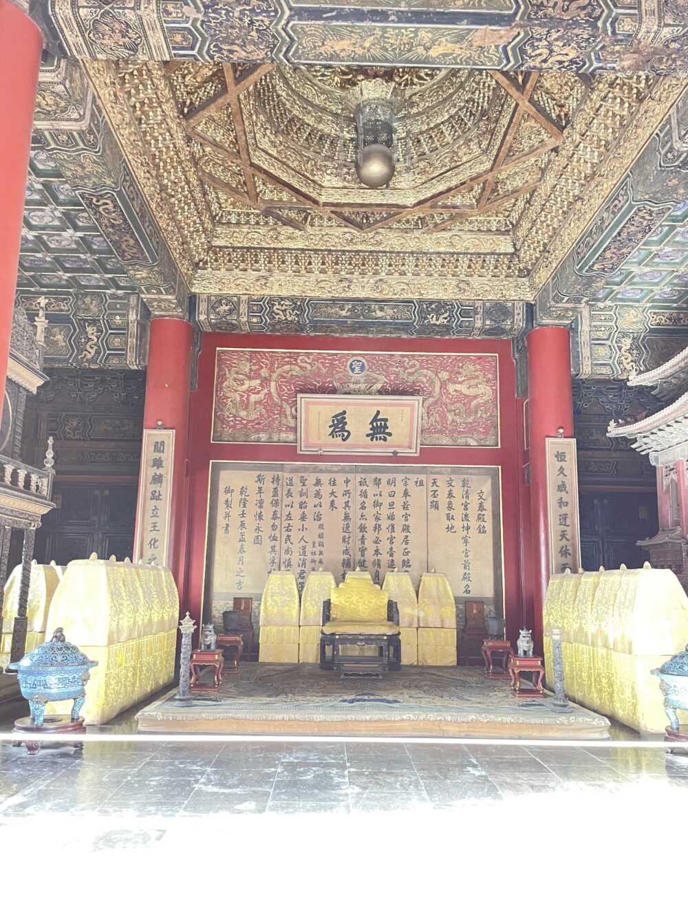 交泰殿の内部。金色に輝く皇后の玉座と、その上部に精緻な装飾が施された八角形の藻井が広がり、壁面には漢字の詩文が整然と並ぶ格式高い空間。