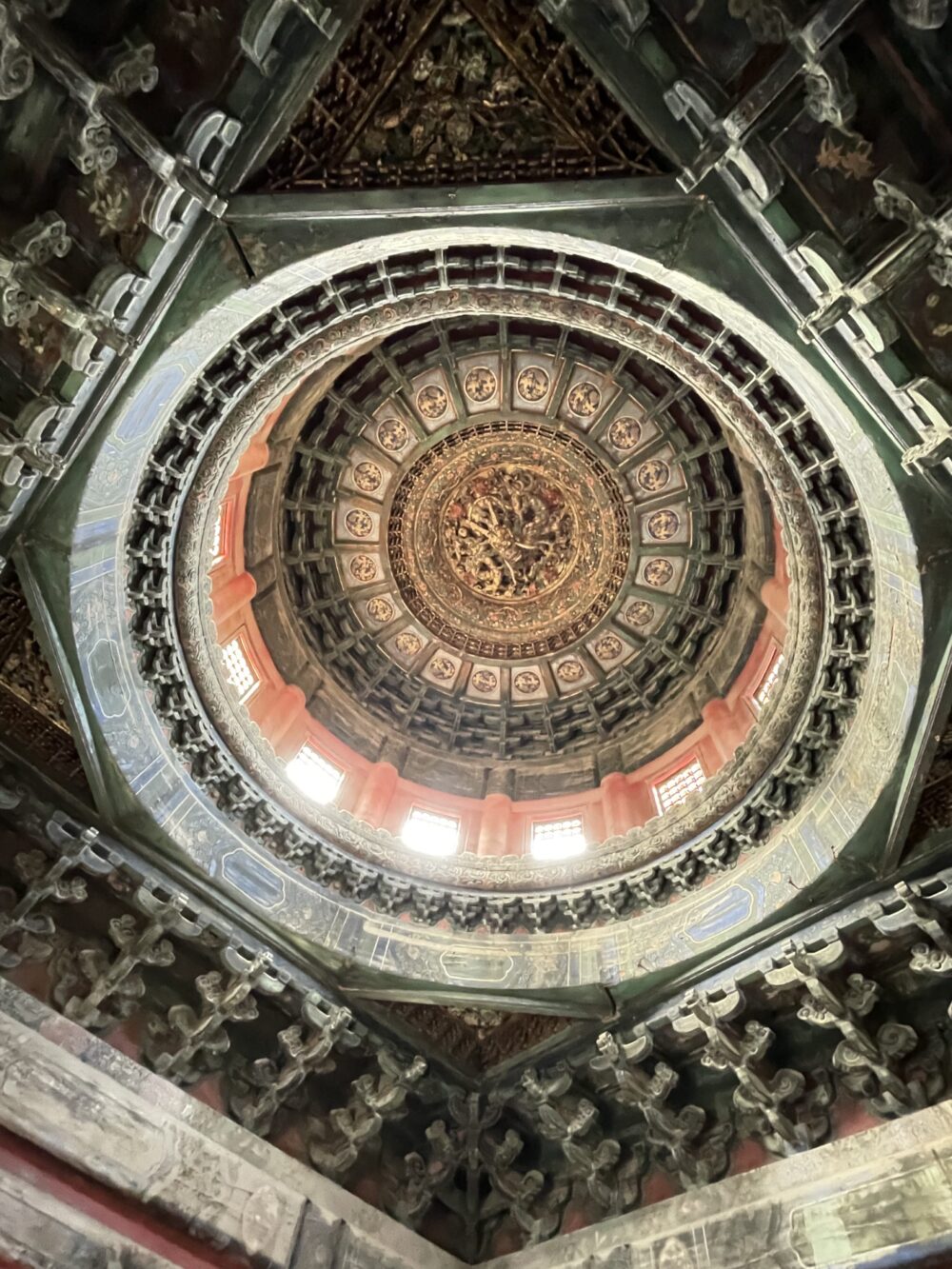 万春亭内部の天井を真上から見上げた様子。重層的に組まれた斗拱が円形に広がり、中央には金色の龍が彫られた豪華な藻井が輝く。