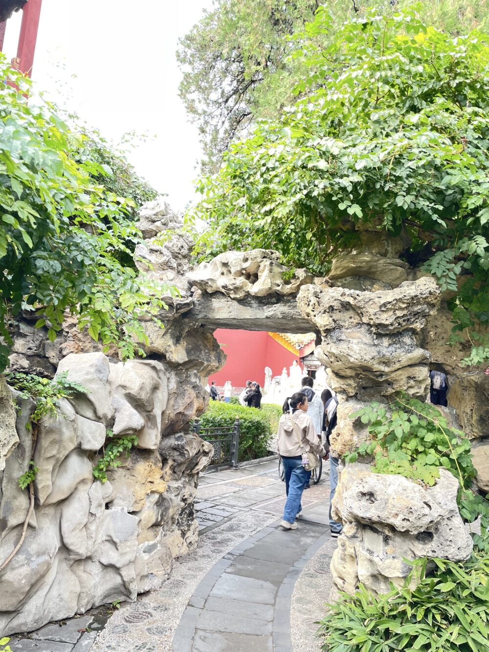 御花園の假山に設けられた小さな洞門。太湖石で組まれた自然石のアーチを、人々が順路に沿ってくぐり抜けていく様子。