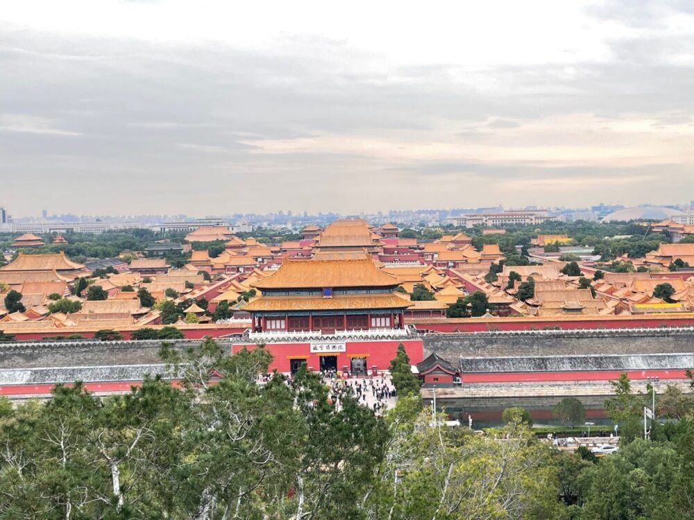 景山公園の展望エリアから望む故宮・紫禁城の全景。北門（神武門）を正面に、黄金色の宮殿群が奥へと連なり、北京の街並みまで見渡せる雄大な風景。