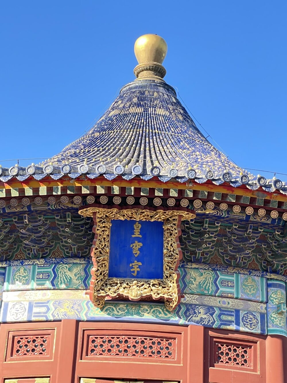 北京・天壇公園の皇穹宇。青瓦屋根と金色の宝頂、龍と雲文様、斗拱（ときょう）が重なる精緻な装飾と青い扁額が特徴の明清時代の祭祀建築