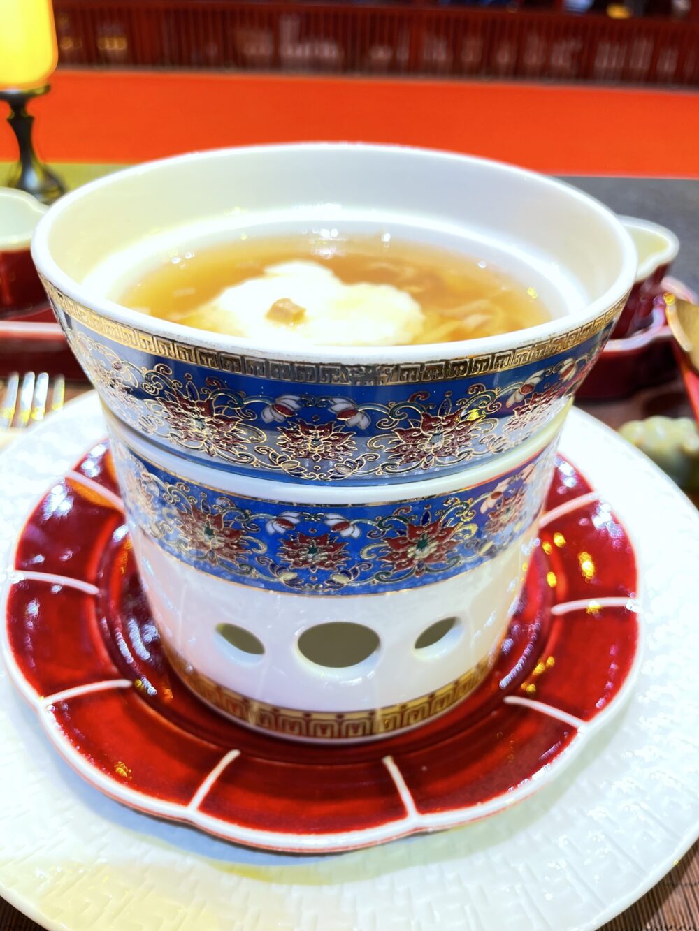 北京御仙都皇家庭菜の宮廷風麺料理。青と金の花紋装飾が施された透かし器に盛られた澄まし仕立ての一椀。