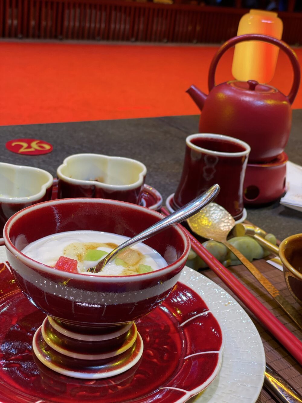 北京御仙都皇家庭菜の宮廷ランチのデザート。赤い磁器の器に盛られたフルーツ入りヨーグルトと宮廷風テーブルセッティング。