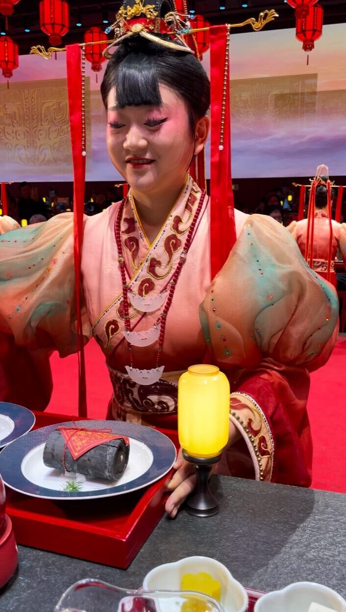 北京御仙都皇家庭菜での宮廷晩餐ショー。清朝風衣装の女性パフォーマーが料理を運ぶ幻想的な演出。