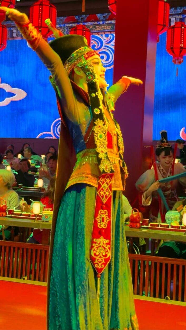 民族衣装をまとった女性ダンサーが、赤提灯の下で両腕を広げて舞う舞台パフォーマンス。