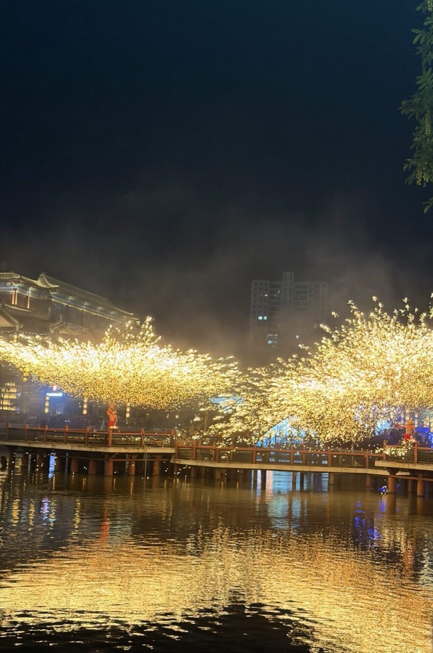 横店影視城・清明上河図で上演される打鉄花。夜の水辺に黄金色の火花が扇状に広がり、水面にも幻想的な光が映り込む様子