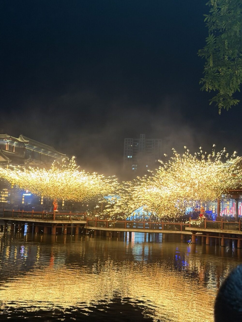横店影視城・清明上河図で上演される打鉄花。夜の水辺に黄金色の火花が扇状に広がり、水面にも幻想的な光が映り込む様子