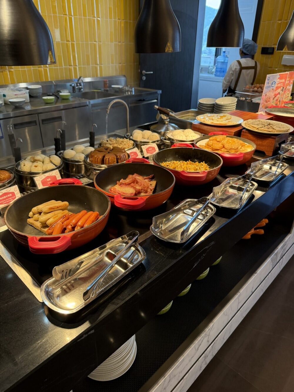 ライブキッチン周辺の朝食ビュッフェ。点心や炒飯、ソーセージなどの温かい料理が並ぶ