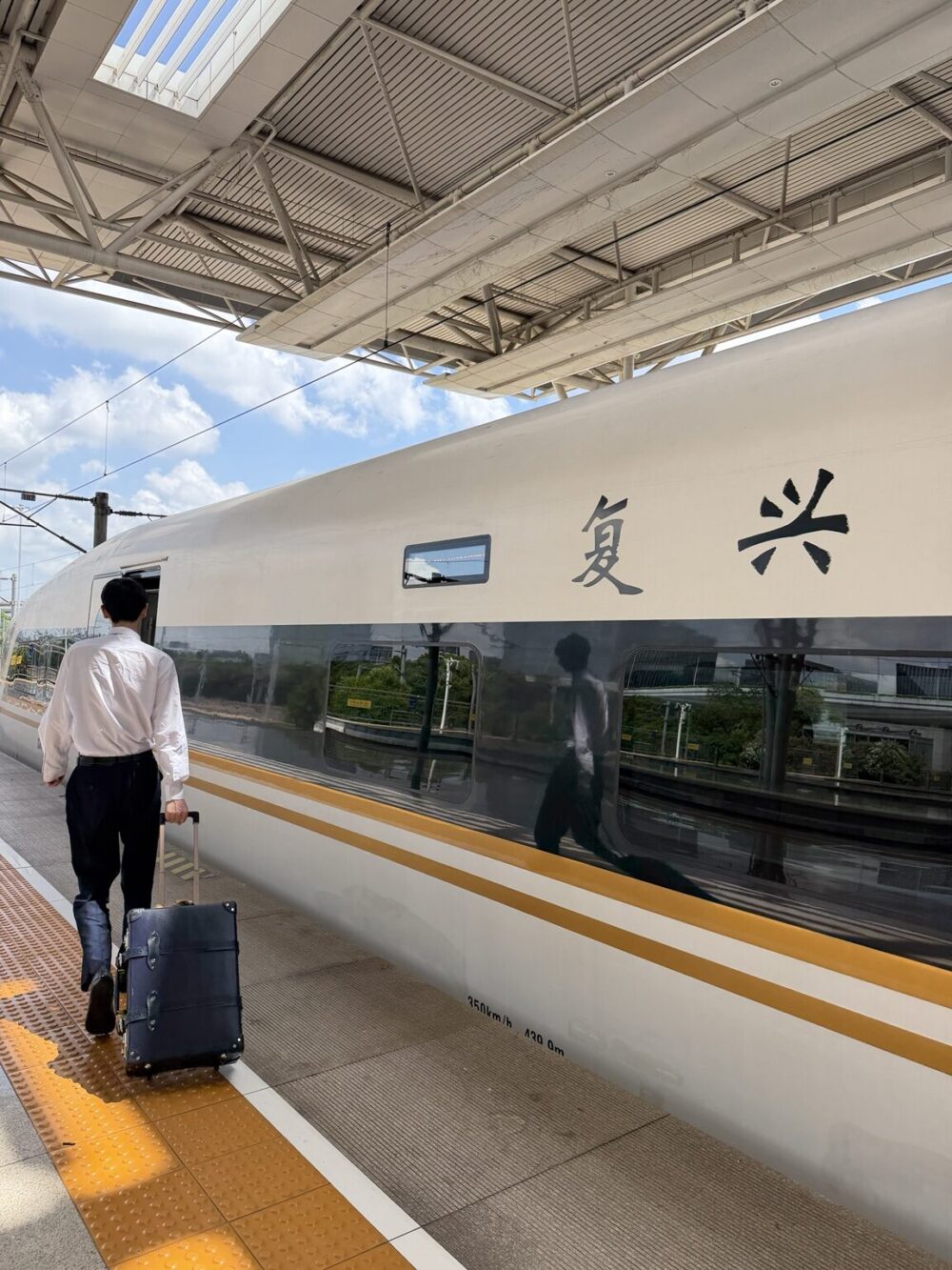 横店駅ホームに停車する高速鉄道と、スーツケースを引いて乗車する駅スタッフ